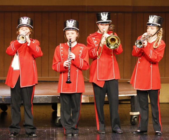 Five young musicians in marching band uniforms on stage.