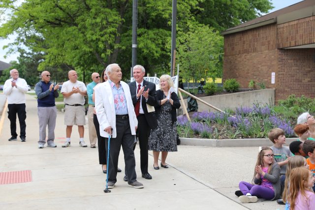 Older couple receiving applause, people clapping, outdoor setting, event, community gathering, celebration, awards ceremony.