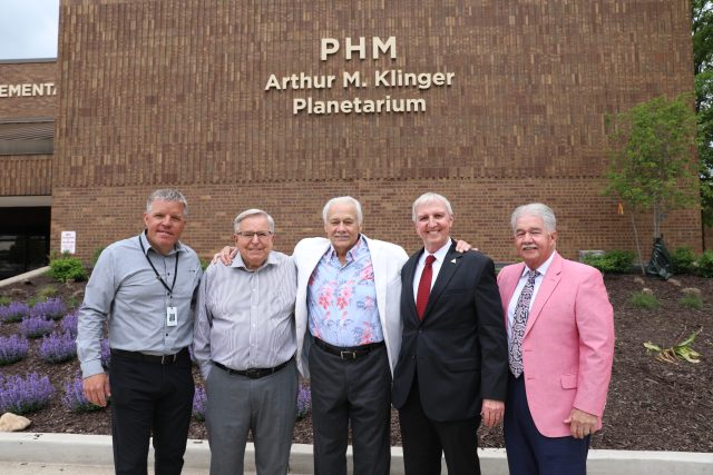 Five men standing in front of a brick building with a sign that reads "PHM" and "Arthur M. Klinger Planetarium".