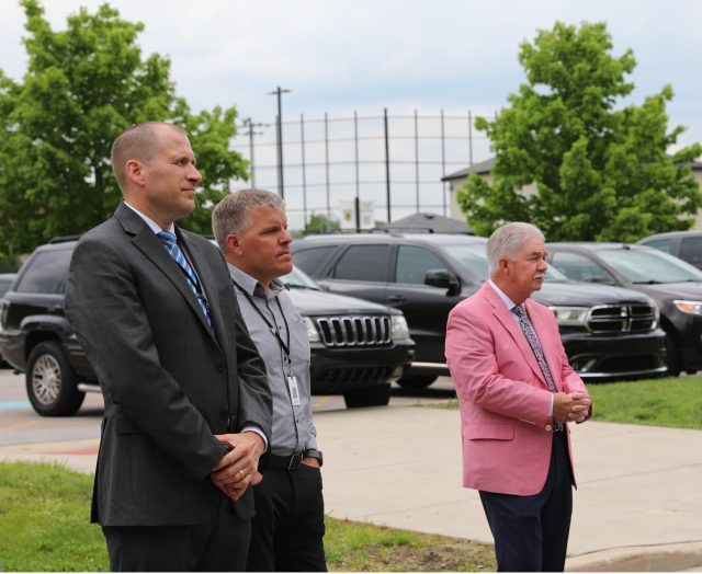 Three men standing in front of a row of parked cars.