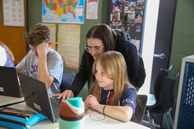 teacher helping student at a laptop