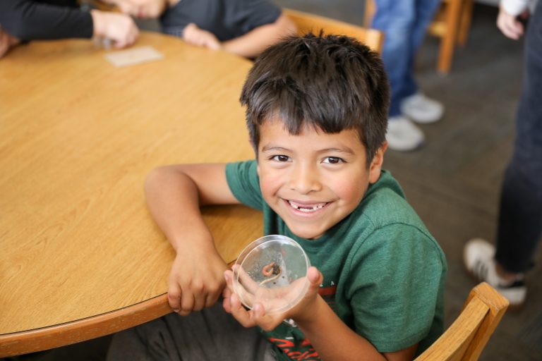 Boy holding a small glass dome at a table in a room.