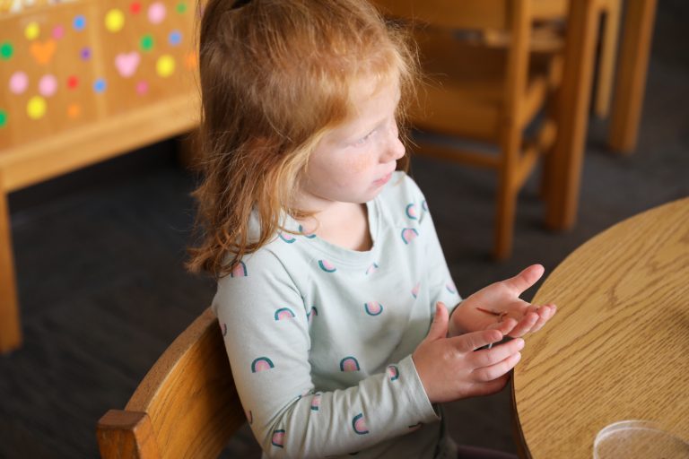 Young girl sitting at a table in a restaurant, looking down at her hands clasped together.