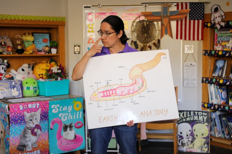 Woman holding a sign with a diagram of an animal in front of a room full of books and toys.