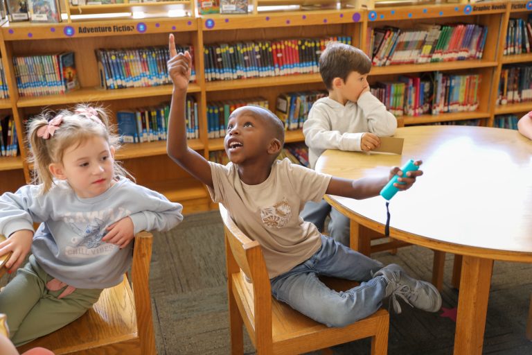 Children in a library, sitting at tables, looking at books.