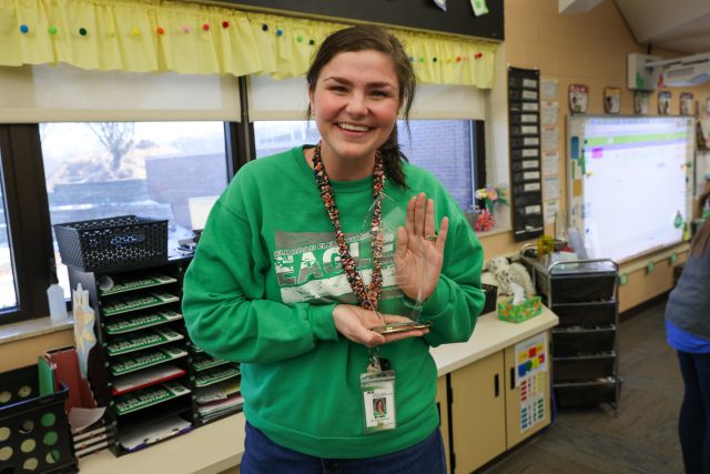 A woman in a classroom holding an award.