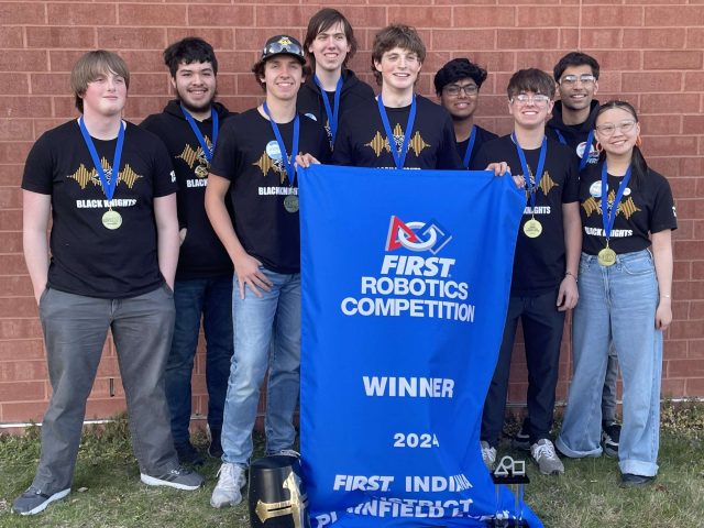 Team of robotics competition winners posing for a picture in front of their trophy.