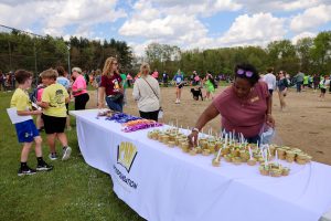 This is a color photograph showing an outdoor event where people are gathered around a table covered with items for sale or